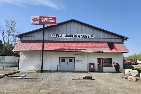 Exterior of W.J. Lambert & Sons building with a Massey Ferguson sign on top, showcasing the dealership storefront under a clear blue sky.
